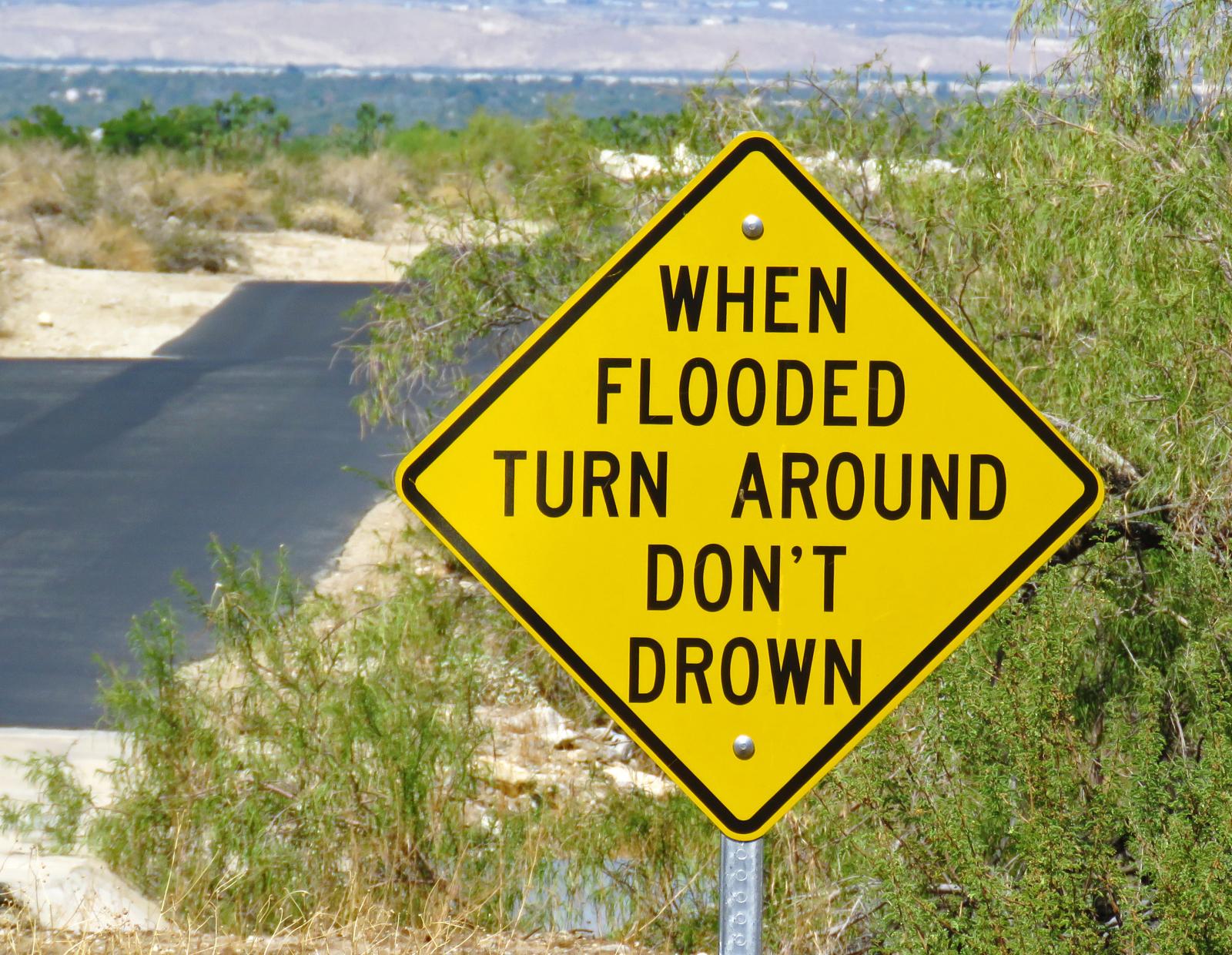 Stock image of a yellow, diamond-shaped road sign that reads "WHEN FLOODED TURN AROUND DON'T DROWN"