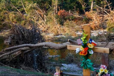 A cross at a memorial in Guadalupe Park is seen near downed trees in the Guadalupe River from the July 4 floods, Friday, July 25, 2025, in Kerrville, Texas. While we cannot erase tragedies, we can use our knowledge and research to improve preparedness, warnings and response, writes David R. Maidment. Photo by Elías Valverde II, Dallas Morning News staff photographer